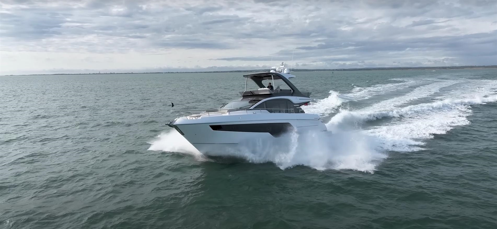 A luxury motor yacht speeds through the ocean, creating white spray against a cloudy sky.